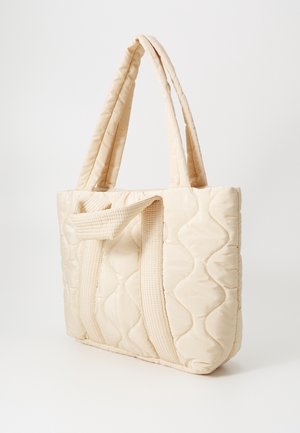 Sac cabas matelassé beige avec deux anses en tissu texturé, présentant une surface lisse et un motif ondulé pour plus de détails.
