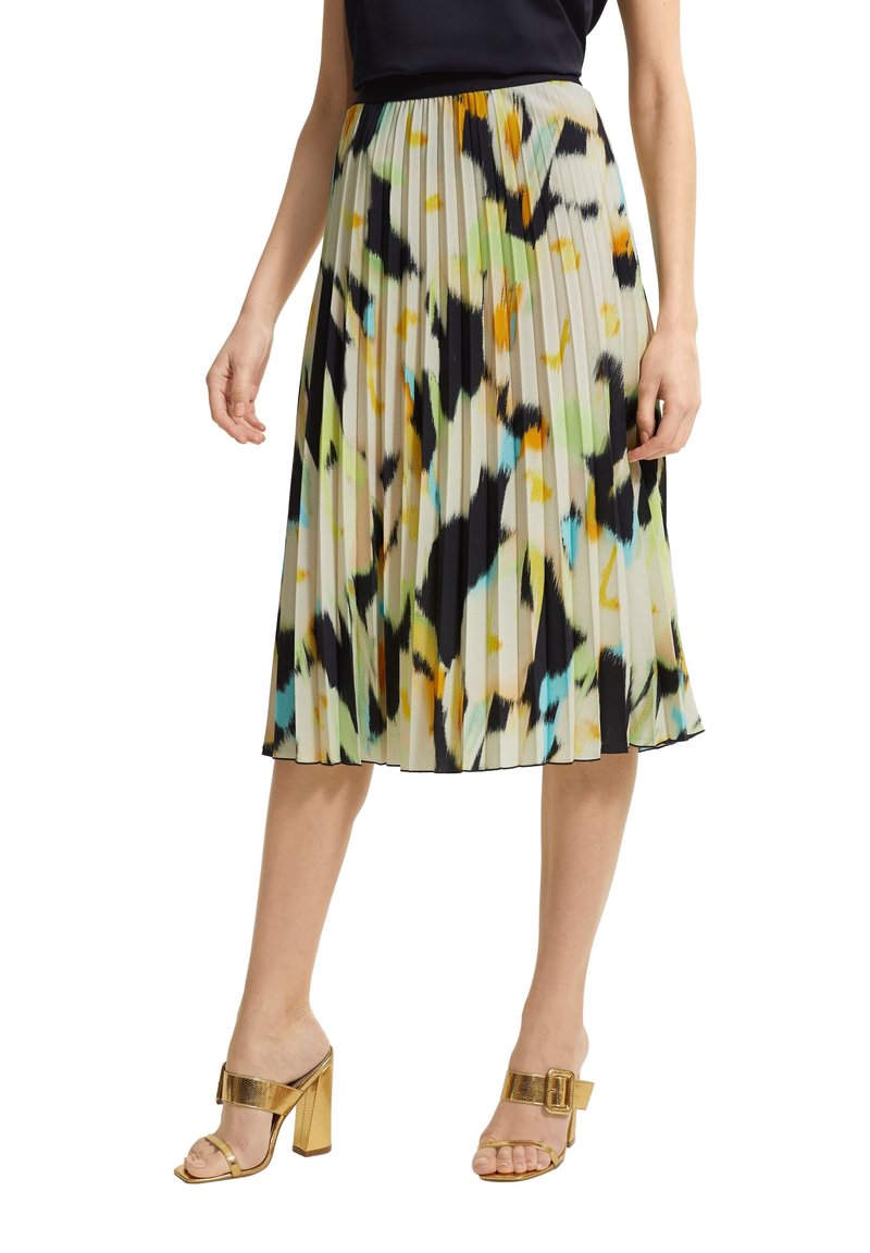 Falda midi plisada de un vibrante patrón abstracto en verdes, negros y naranjas, hecha de una tela ligera. Combinada con tacones de bloque dorados.