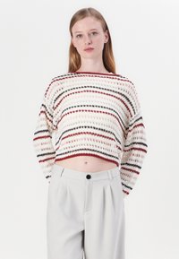 Crocheted sweater with a loose fit, featuring horizontal stripes in red, black, and cream. Paired with light gray high-waisted pants.