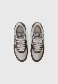 Nike tenisice s gornjim dijelom od mrežastog materijala u sivoj i smeđoj boji, s teksturiranim dizajnom, kontrastnim vezicama i logotipom na jeziku.