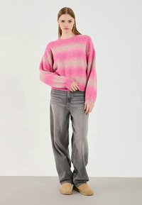 Maglione a righe rosa e beige in morbido knit, vestibilità rilassata, con scollatura a girocollo. Abbinato a jeans baggy grigi sbiaditi e pantofole color marrone chiaro.