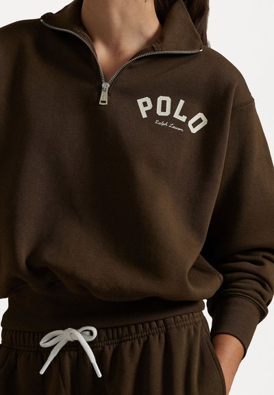 Καφέ φούτερ με φερμουάρ και ριγέ λαιμό, με λευκή εκτύπωση "POLO" και λεπτομέρεια με κορδόνι στη μέση. Μαλακό, υφασμάτινο υλικό.