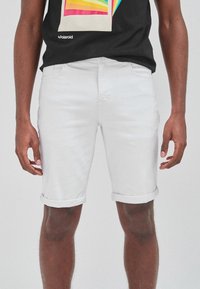 Shorts de mezclilla blanca con dobladillos enrollados, que presentan un diseño ajustado y una textura sutil, combinados con una camiseta gráfica negra.