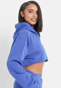 Korte hoodie van effen blauwe stof met een capuchon, wijde mouwen en een relaxte pasvorm. Verfraaid met een klein logo aan de voorkant.