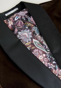 Black blazer with a satin floral lining featuring shades of purple, pink, and green. Smooth texture with a sharp lapel design.