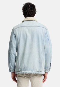 Ljusblå denimjacka med en krage i konstpäls, synlig sömnadsdetalj och elastisk nederkant. Har en avslappnad passform och långa ärmar.