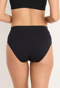 Svart högmidjad trosor med en slät textur, elastisk midja och en sömlös finish vid benöppningarna.