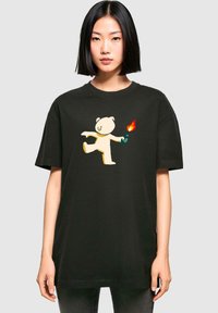 Juodas per didelis t-shirt pagamintas iš medvilnės, su žaismingu baltu lokio grafiniu atvaizdu, laikantiu ugnį. Trumpi rankoviai ir apvalus kaklo dizainas.