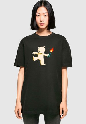 Black oversized t-shirt made of cotton, featuring a playful white bear graphic holding a flame. Short sleeves and round neck design.