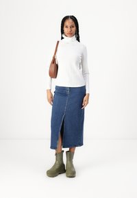 Valge soonikuline kõrge kaelusega särk, denim midi-seelik esiõhuga ja oliivirohelised pahkluu saapad. Pruun õlakott täiendab riietust.