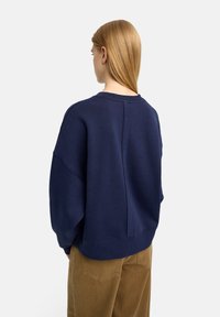 Granatowy oversize'owy sweter z okrągłym dekoltem, opadającymi ramionami i detalem szwu z tyłu. Miękka tkanina o teksturowanym wykończeniu.