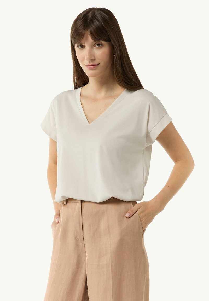Krótki rękaw, top z dekoltem w serek w jasnobeżowym kolorze, charakteryzujący się luźnym krojem i gładką teksturą, zestawiony z beżowymi spodniami lnianymi.