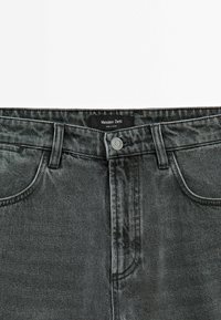 Dark gray denim jeans with a classic five-pocket design and a standard button closure. Black brand label visible at the waistband.
