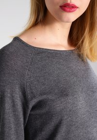 Haut gris à manches longues en tissu doux avec un encolure large et une texture lisse. Présente un design simpliste avec des détails de couture minimaux.