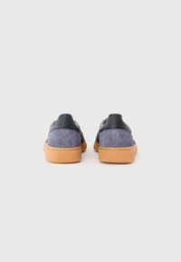 Sapatilhas de camurça roxas com uma sola de borracha texturizada e accents verde escuro no calcanhar, apresentando um design minimalista e entrada sem atacadores.