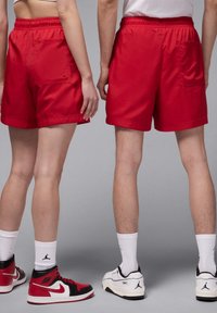 Rote Shorts mit einem elastischen Bund und Seitentaschen, die eine glatte Textur und einen leicht lockeren Schnitt aufweisen, kombiniert mit kontrastierenden Schuhen.