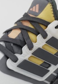 Gros plan des lacets noirs sur une basket jaune et noire avec une cage de soutien blanche et trois bandes noires sur le côté.