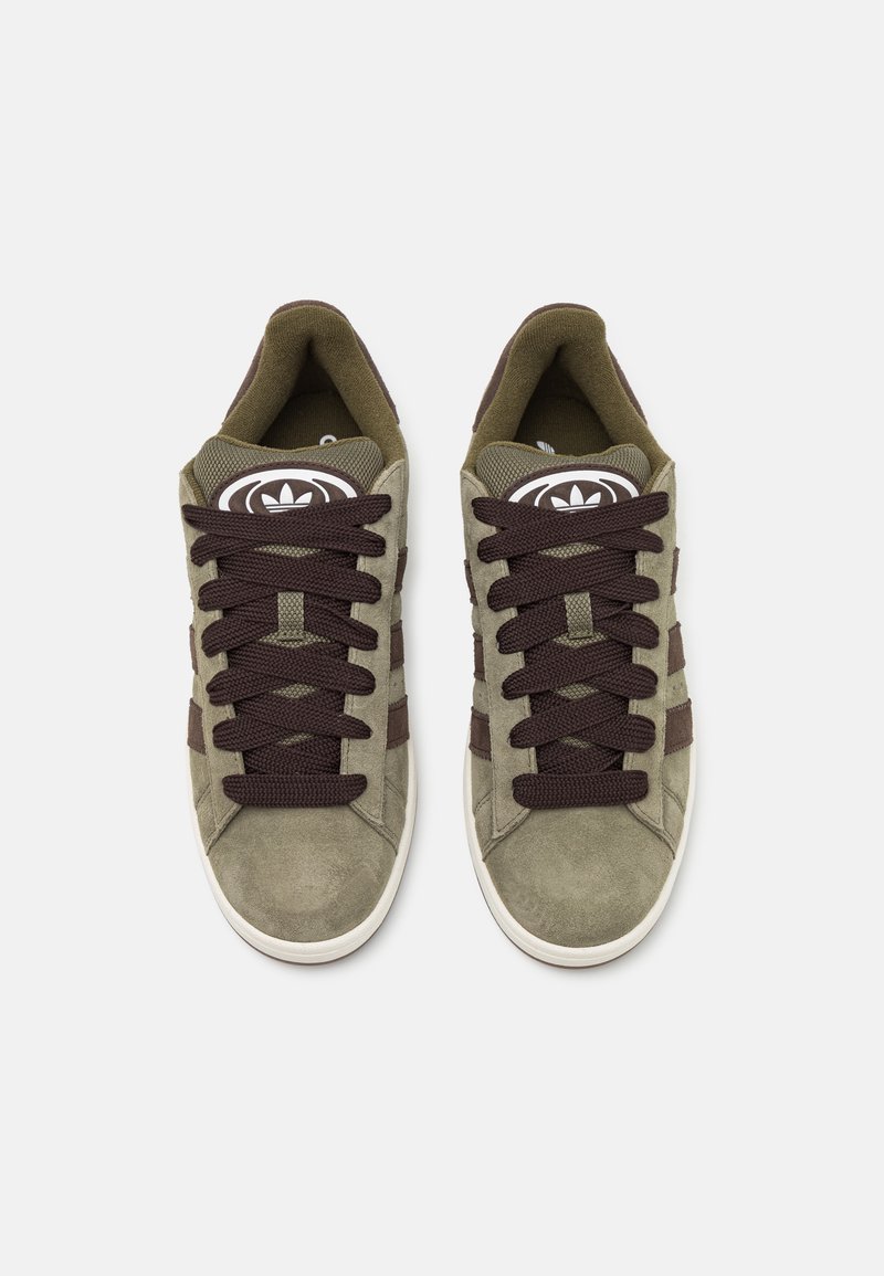 Des baskets en suede vert avec des lacets et des accents marron foncé, présentant un logo blanc sur la languette et trois bandes marron sur les côtés.