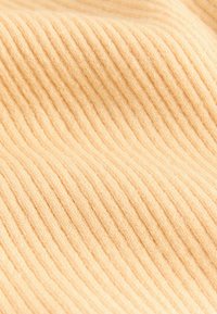 Ribbed fabric in soft peach color, showing textured lines that create a vertical pattern. Material appears cozy and lightweight.