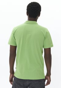 Grön bomullspolo med korta ärmar och krage. Har raka slag och är ihopparad med gråa shorts. Enkel, enfärgad design.