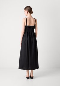 Robe maxi noire sans manches avec un corsage froncé, des fines bretelles et une jupe fluide. Tissu lisse et léger avec une coupe décontractée.