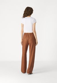 Pantalon large en lin beige avec une taille élastique, associé à un haut ajusté à manches courtes blanc. Texture lisse, design décontracté.