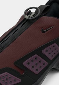 Nike tenisice s bordo gornjom stranom s teksturiranim završetkom, crnim detaljima i ljubičastim gumenim umetkom s ventilacijskim rupama.