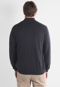 Grosse veste zippée grise foncée, en tissu tricoté doux, avec un col et des poignets côtelés, un ourlet élastique, affichant un logo subtil sur l'épaule.