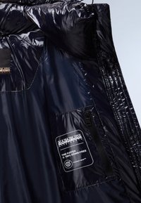 Giacca puffer blu navy con un'esterno lucido e liscio, dotata di una tasca con zip e un'etichetta che indica un'isolamento 100% privo di piume.