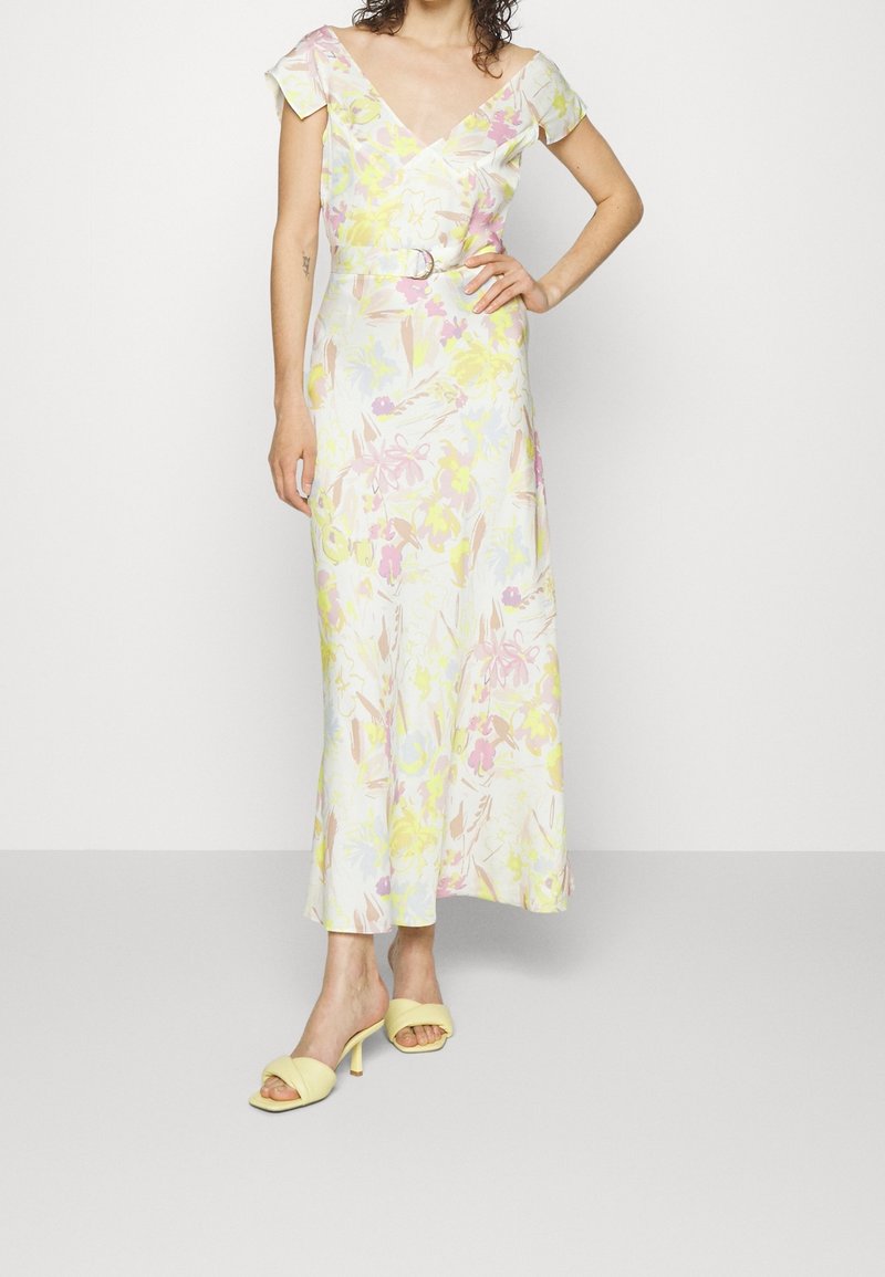 Bloemenmidi-jurk in wit, met pastelroze, gele en blauwe patronen, kapmouwen en een tailleceintuur. Gecombineerd met gele sandalen met hak.