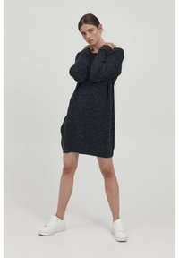 Robe tricotée bleu marine foncé à manches longues et à coupe décontractée, avec un col rond et des poches latérales, associée à des baskets blanches.