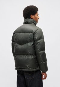 Zelena pufasta jakna s visokim ovratnikom, prošivenim uzorkom i glatkom teksturom; ima elastične manžete i ravni rub.