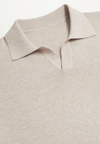 Pull en beige à col avec un décolleté en V, fait de tissu texturé, comportant un col lisse et un motif côtelé subtil sur l'ensemble.