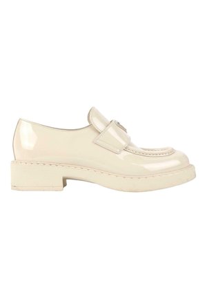 Mocassin en cuir verni couleur crème avec une semelle épaisse et une bride sur le dessus, présenté de côté sur fond blanc.