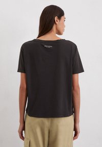Dunkelgraues, kurzärmliges T-Shirt aus Baumwolle, mit lockerer Passform und leicht gesenktem Schulterbereich. Auf der Rückseite ist ein kleines Markenlogo abgebildet.