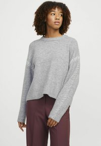Pull en tricot gris avec un col rond, un design court et des coutures contrastées le long des manches. Texture douce avec des poignets côtelés.