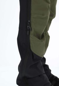 Czarne i oliwkowozielone spodnie z kieszeniami na zamek, wykonane z trwałej tkaniny. Charakteryzują się zwężanym krojem i teksturowanymi panelami zapewniającymi wentylację.