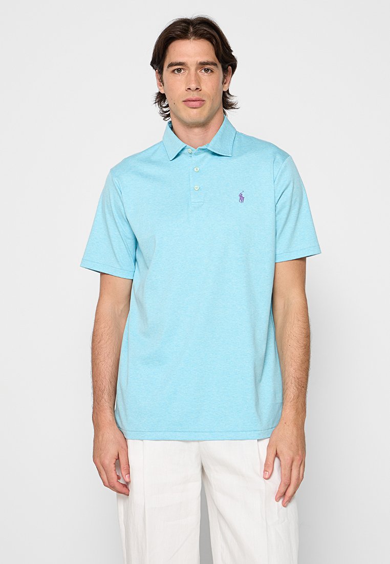 Jasnoniebieska koszula polo wykonana z miękkiego materiału, z krótkim kołnierzykiem, trzema guzikami oraz małym fioletowym logo na lewej stronie klatki piersiowej.