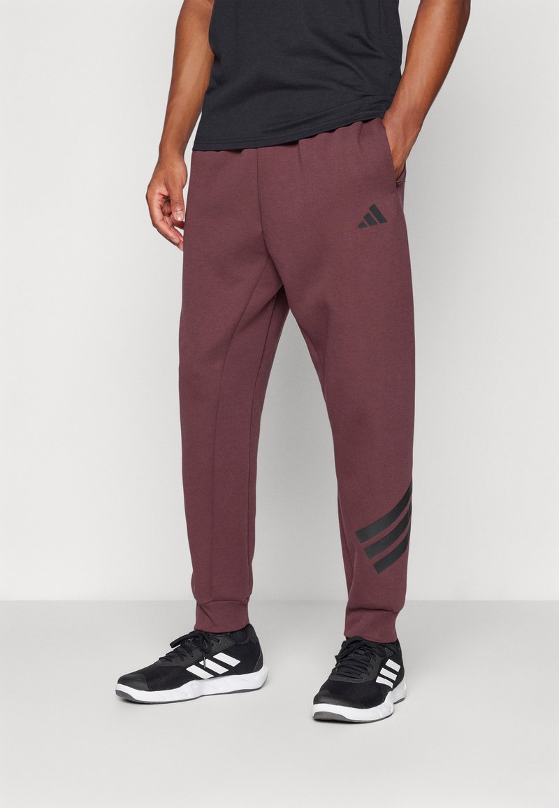 Bordeauxrode sweatpants van zacht materiaal met geribde boorden. Kenmerkt zich door het zwarte Adidas-logo en drie zwarte strepen op het linkerpijpen.