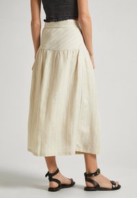 Vaaleanbeige, polvipituinen hame, jossa on ohuita valkoisia raitoja, korkeavyötäröinen muotoilu ja rypistetty helma. Yhdistetty mustiin sandaaleihin, joissa on nilkkahihnat.