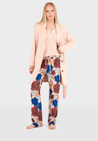 Cardigan rosa testurizzato sopra una maglia chiara e pantaloni da pigiama floreali multicolori. I pantaloni presentano fiori blu e rossi su uno sfondo chiaro.
