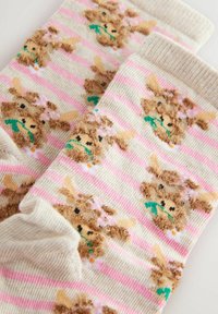 Stricksocken mit einem gestreiften Muster und braunen Hasenmotiven, akzentuiert von rosa Blumen, grünen Blättern und einer weichen, flauschigen Textur.
