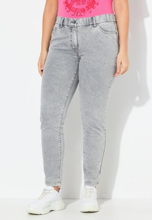 Hellgraue Denim-Skinny-Jeans mit mittelhohem Bund, Frontknopfverschluss und Gesäßtaschen, kombiniert mit weißen Sportschuhen.