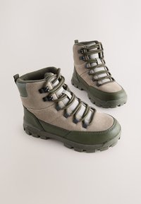 Grüne und beige Wanderschuhe mit Wildleder-Obermaterial, profilierter Gummisohle, Metallösen und gepolstertem Kragen für Komfort.