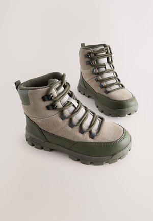 Botas de senderismo verdes y beige con parte superior de ante, suela de goma texturizada, ojales metálicos y un cuello acolchado para mayor comodidad.