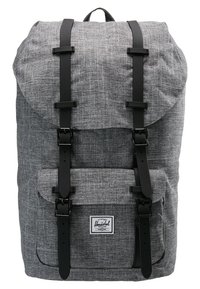 Szary plecak z tkaniny z czarnymi paskami na klamry, przednią kieszenią oraz białą prostokątną metką marki na klapie kieszeni.