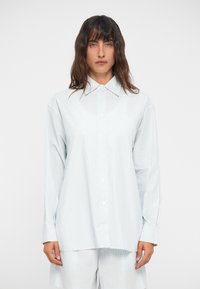 Απαλό μπλε ριγέ πουκάμισο με κλασικό γιακά, μακρύ μανίκι και άνετη εφαρμογή. Το ύφασμα φαίνεται απαλό, με κατακόρυφες ρίγες.