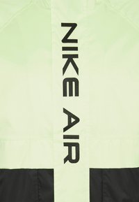 Ljusgrön nylonjacka med svart "NIKE AIR" broderi längs mitten. Slät textur med en kontrasterande svart nedre del.