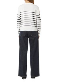 Wit gebreid sweater met zwarte horizontale strepen, gecombineerd met donkerblauwe wijde jeans. Beschikt over een ronde halslijn en geribde manchetten.