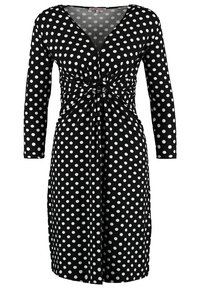 Svart klänning med vita prickar, långa ärmar, V-ringning, rynkad midja med en vriden knut, knälång design. Slät tygtextur.